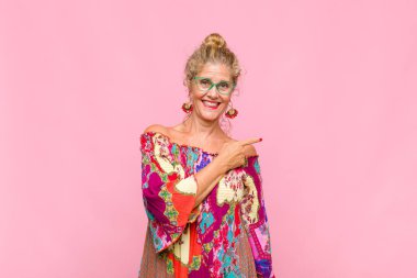 Orta yaşlı kadın neşeli bir şekilde gülümsüyor, mutlu hissediyor ve yan ve yukarı doğru işaret ediyor, fotokopi uzayındaki nesneleri gösteriyor.