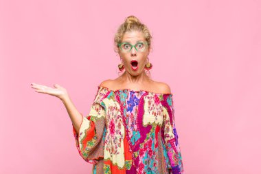 Orta yaşlı kadın şaşırmış ve şoka uğramış görünüyor, çenesi düşmüş ve eli açık bir nesneyi tutuyor.