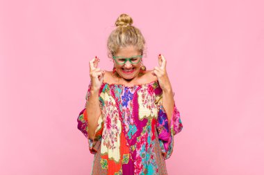 Orta yaşlı kadın gülümsüyor ve endişeyle iki parmağını çapraz yapıyor. Endişeli hissediyor, iyi şanslar diliyor ya da umut ediyor.