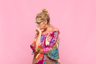 Orta yaşlı kadın ciddi, düşünceli ve endişeli, elleri çenesine bastırılmış bir şekilde yan bakıyor.