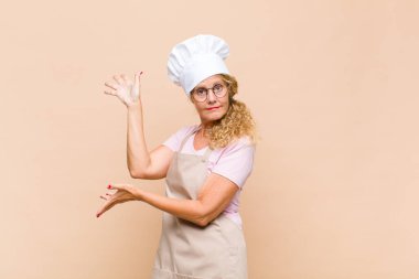 Orta yaşlı fırıncı gururla gülümsüyor, mutlu ve tatmin olmuş hissediyor ve fotokopi alanında bir konsept gösteriyor.