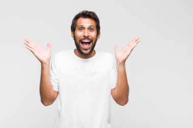Genç Latin yakışıklı adam gururlu, kendinden emin ve mutlu görünüyor, gülümsüyor ve kendini işaret ediyor ya da bir numara işareti yapıyor.