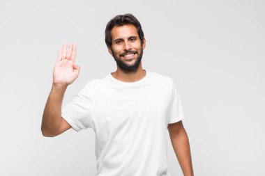 Genç Latin yakışıklı adam mutlu ve neşeyle gülümsüyor, el sallıyor, seni selamlıyor ya da veda ediyor.