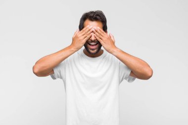 Genç Latin yakışıklı adam gülümsüyor ve mutlu hissediyor, iki eliyle gözlerini kapatıyor ve inanılmaz bir sürpriz bekliyor.