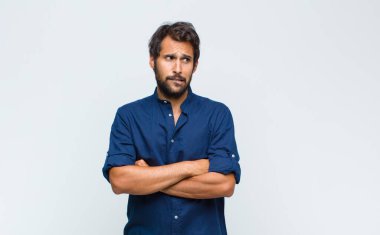 Genç Latin yakışıklı adam şaşkın ve şaşkın hissediyor, şüpheci, ağırlıklı ya da farklı seçenekleri komik bir ifadeyle seçiyor