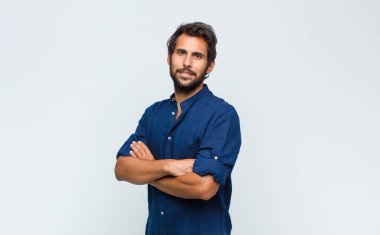 Genç Latin yakışıklı adam mutlu bir şekilde gülümsüyor, eli kalçasında ve kendinden emin, olumlu, gururlu ve arkadaş canlısı.
