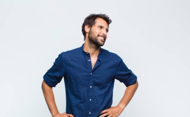 Genç Latin yakışıklı adam mutlu bir şekilde gülümsüyor ve hayal kuruyor ya da şüphe ediyor.