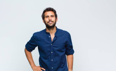 Genç Latin yakışıklı adam utangaç ve neşeli bir şekilde gülüyor, arkadaş canlısı ve olumlu ama güvensiz bir tavırla.