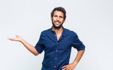 Genç Latin yakışıklı adam gülümsüyor, mutlu, kaygısız ve tatmin olmuş hissediyor, fotokopi alanındaki konsepte veya fikre işaret ediyor.