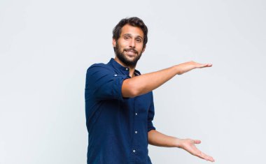 Genç Latin yakışıklı adam mutlu bir şekilde gülümsüyor, arkadaş canlısı, kendinden emin, olumlu bakışlı, bir nesne ya da konsept sunuyor ve gösteriyor.