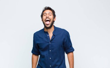 Genç Latin yakışıklı adam mutlu, heyecanlı ve pozitif hissediyor. Elleri ağızda, bağırıyor.