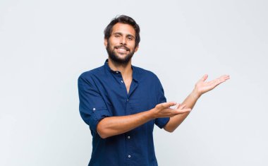 Genç Latin yakışıklı adam neşeyle gülümsüyor sıcak, dostça, sevgi dolu bir kucak veriyor, mutlu ve sevimli hissediyor.