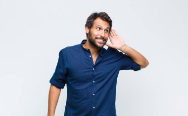 Genç Latin yakışıklı adam şaşkın ve şaşkın bakıyor, el üstünde uzak bakıyor, izliyor ya da arıyor