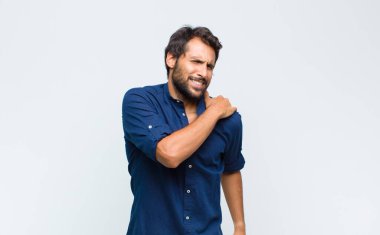 Genç Latin yakışıklı adam üzgün, yaralı ve kalbi kırık görünüyor, iki elini de kalbine yakın tutuyor, ağlıyor ve depresif hissediyor.