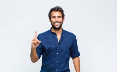 Genç Latin yakışıklı adam gülümsüyor ve arkadaş canlısı görünüyor, iki ya da iki numarayı gösteriyor, eli önde, geriye doğru sayıyor.