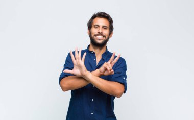 Genç Latin yakışıklı adam gülümsüyor ve arkadaş canlısı görünüyor, 8 ya da 8 numarayı gösteriyor, eli önde, geri sayıyor.