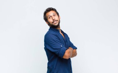 Genç Latin yakışıklı adam neşeyle gülümsüyor, mutlu, tatmin olmuş ve rahatlamış hissediyor, kollarını kavuşturup yan tarafa bakıyor.