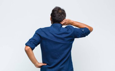 Genç Latin yakışıklı adam düşünüyor ya da şüphe ediyor, kafasını kaşıyor, kafası karışık ve kafası karışık, arkaya ya da arkaya bakıyor.