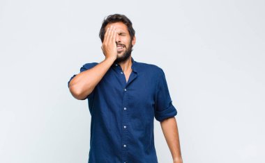 Genç Latin yakışıklı adam uykulu görünüyor, sıkılmış ve esniyor, baş ağrısı ve yüzünün yarısını kaplayan bir eliyle