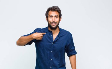 Genç Latin yakışıklı adam mutlu, gururlu ve şaşırmış görünüyor, neşeli bir şekilde kendini gösteriyor, kendinden emin ve yüce hissediyor.