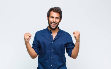 Genç Latin yakışıklı adam mutlu, şaşırmış ve gururlanmış hissediyor, bağırıyor ve başarıyı büyük bir gülümsemeyle kutluyor.