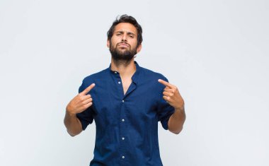 Kötü tavırlı genç Latin yakışıklı adam gururlu ve agresif görünüyor, yukarıyı işaret ediyor ya da elleriyle alay işareti yapıyor.