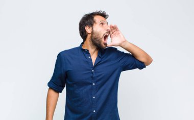 Genç Latin yakışıklı adam öfkeyle bağırıyor kenardaki boşluğu kopyalasın diye, eli ağzının yanında.