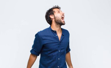 Genç Latin yakışıklı adam öfkeyle bağırıyor, agresif bir şekilde bağırıyor, stresli ve sinirli görünüyor.