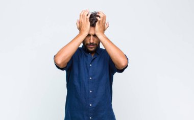 Genç Latin yakışıklı adam stresli ve endişeli, depresif ve hayal kırıklığına uğramış hissediyor, iki elini de başa kaldırıyor.