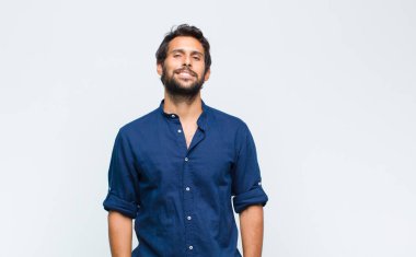 Genç Latin yakışıklı adam neşeli ve tesadüfen gülümsüyor pozitif, mutlu, kendinden emin ve rahat bir ifadeyle