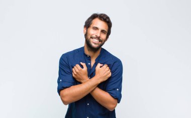 Genç Latin yakışıklı adam neşeyle gülümsüyor ve kutluyor, yumruklarını sıkıp kollarını kavuşturuyor, mutlu ve pozitif hissediyor.