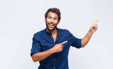 Genç Latin yakışıklı adam, neşeli ve şaşırmış hissediyor, şok olmuş bir ifadeyle gülümsüyor ve bir tarafı işaret ediyor.