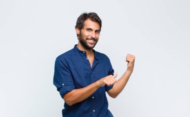 Genç Latin yakışıklı adam neşeyle gülümsüyor ve yan taraftaki fotokopi alanını gösteriyor, mutlu ve tatmin olmuş hissediyor.