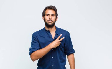 Genç Latin yakışıklı adam kendini mutlu, pozitif ve başarılı hissediyor. Göğsünde V şeklinde eller yapıyor. Zafer ya da barış gösteriyor.
