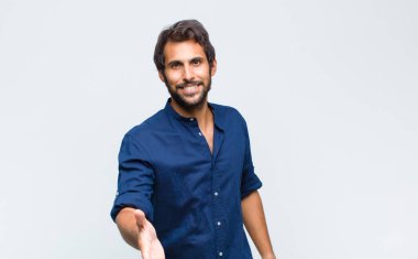 Genç Latin yakışıklı adam gülümsüyor, mutlu, kendinden emin ve arkadaş canlısı görünüyor, bir anlaşma yapmak için el sıkışmayı teklif ediyor, işbirliği yapıyor.