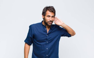 Genç Latin yakışıklı adam ciddi ve meraklı görünüyor, dinliyor, gizli bir konuşma veya dedikodu duymaya çalışıyor, kulak misafiri oluyor.