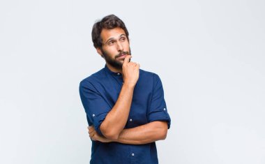 Genç Latin yakışıklı adam düşünceli, meraklı ya da hayal kuruyor, hayal kuruyor ve mekanı kopyalamak için yukarı bakıyor.