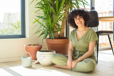 Genç, güzel bir Arap kadın evinde, elinde bir su bidonu ve bitkilerle.