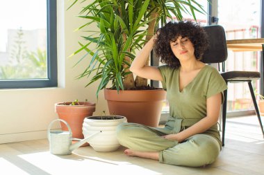 Genç, güzel bir Arap kadın evinde, elinde bir su bidonu ve bitkilerle.