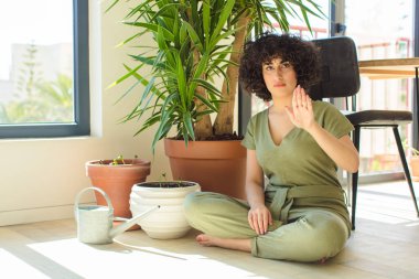 Genç, güzel bir Arap kadın evinde, elinde bir su bidonu ve bitkilerle.