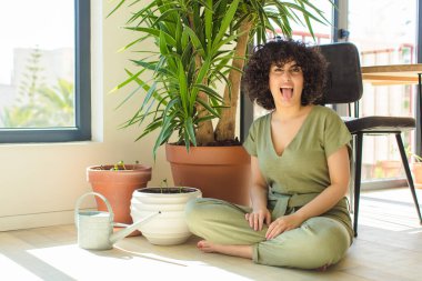 Genç, güzel bir Arap kadın evinde, elinde bir su bidonu ve bitkilerle.