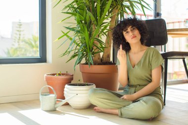 Genç, güzel bir Arap kadın evinde, elinde bir su bidonu ve bitkilerle.