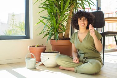 Genç, güzel bir Arap kadın evinde, elinde bir su bidonu ve bitkilerle.