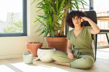 Genç, güzel bir Arap kadın evinde, elinde bir su bidonu ve bitkilerle.