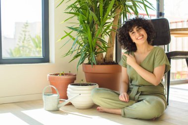 Genç, güzel bir Arap kadın evinde, elinde bir su bidonu ve bitkilerle.