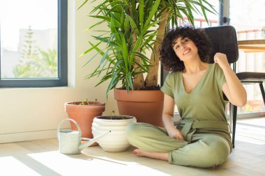 Genç, güzel bir Arap kadın evinde, elinde bir su bidonu ve bitkilerle.