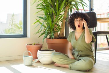 Genç, güzel bir Arap kadın evinde, elinde bir su bidonu ve bitkilerle.