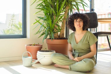 Genç, güzel bir Arap kadın evinde, elinde bir su bidonu ve bitkilerle.