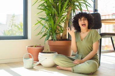 Genç, güzel bir Arap kadın evinde, elinde bir su bidonu ve bitkilerle.