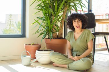 Genç, güzel bir Arap kadın evinde, elinde bir su bidonu ve bitkilerle.